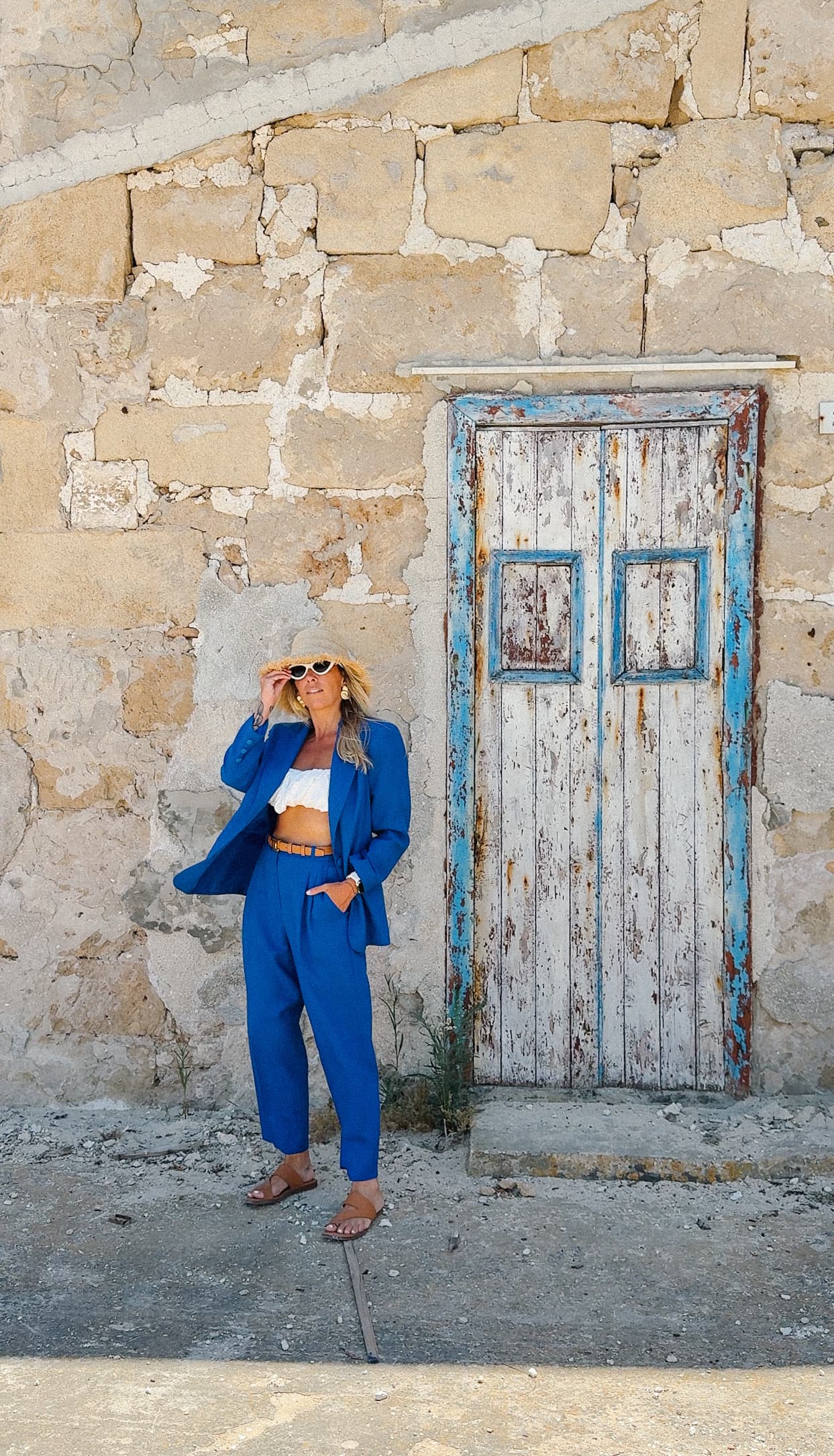 Kat Moore in a blue suit against a rustic Sicilian wall
